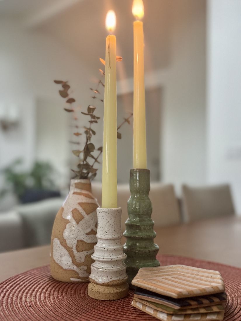 Two ceramic candlesticks in speckled white and ridged moss green with taper candles, a bottle vase and stacked hexagon coasters
