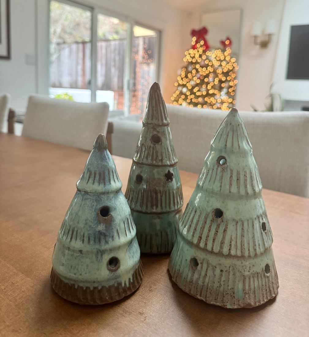 Three seafoam ceramic Christmas trees with pierced holes, on a dining table